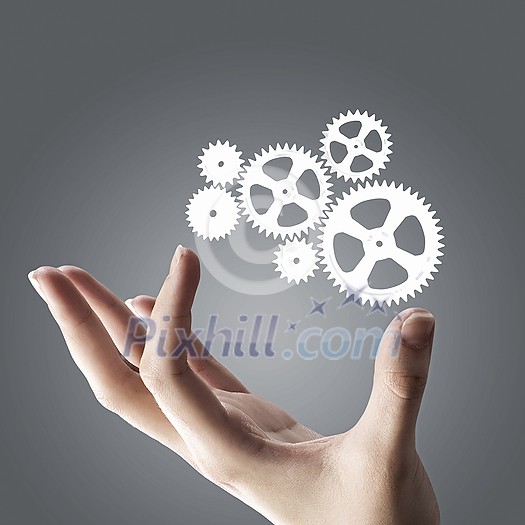 Close up of hand and gears mechanism on gray background Close up of hand and gears mechanism on gray background