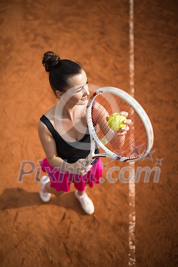 Top view of attractive young woman tennis player serving on a clay tennis court. Interesting POV shot - sporty girl during tennis training in the club Top view of attractive young woman tennis player serving on a clay tennis court. Interesting POV shot - sporty girl during tennis training in the club