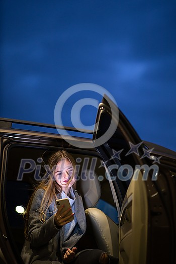 Young woman with her cell phone sitting in the backseat of a car, getting ready to travel (color toned image; shallow DOF)