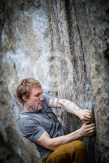 A rock climber climbing on a boulder rock outdoors. Group of friends involved in sports outside.