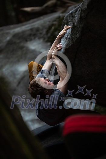 A rock climber climbing on a boulder rock outdoors. Group of friends involved in sports outside.