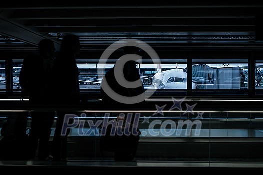 Airport rush: people with their suitcases walking along a corridor (motion blurred image; color toned image)