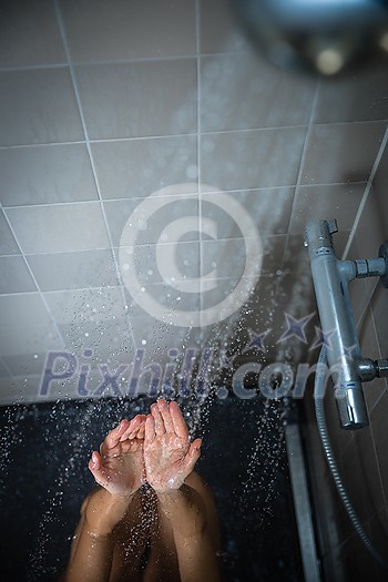 Pretty, young woman taking a long hot shower washing her hair in a modern design bathroom