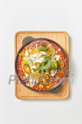 Middle eastern traditional dish Shakshuka from fried eggs with tomatoes, bell pepper, vegetables and herbs in a pan on a wooden board on a light grey background, copy space. Top view.