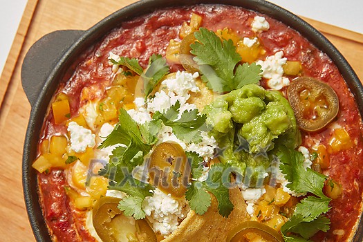 Shakshouka dish homemade from eggs poached in a sauce of tomatoes, olive oil and pepper with common spices in a pan on a wooden board. Middle eastern traditional dish. Shakshouka dish homemade from eggs poached in a sauce of tomatoes, olive oil and pepper with common spices in a pan on a wooden board. Middle eastern traditional dish.