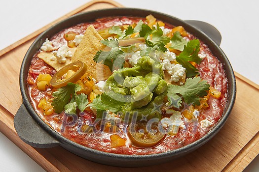 Homemade fresh traditional dish Shakshuka from fried eggs, tomatoes, pepper, vegetables and herbs in a pan on a wooden board on a light grey background, copy space. Middle eastern traditional dish.