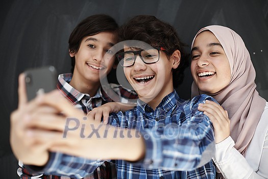 group of arab teens taking selfie photo on smart phone with black chalkboard in background