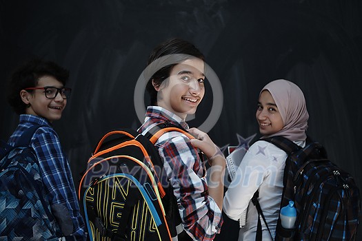 Arabic teenagers, students group portrait against black chalkboard wearing backpack and books in school Arabic teenagers, students group portrait against black chalkboard wearing backpack and books in school