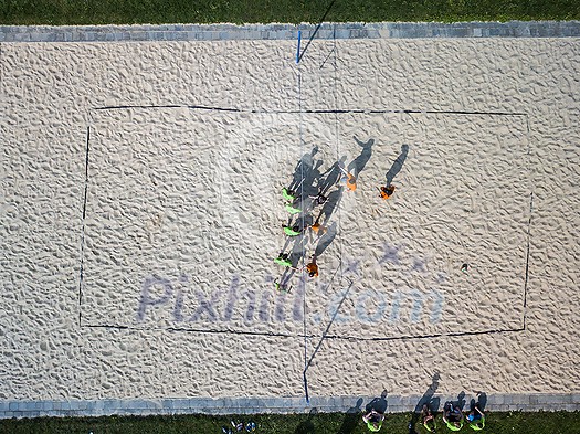 Aerial view of a beach volleyball  pitch with people getting ready for a game in warm morning sun, casting long shadows