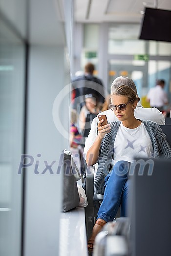 Casual blond young woman using her cell phone while waiting to board a plane at departure gates at international airport.
