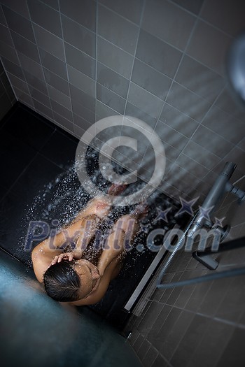 Pretty, young woman taking a long hot shower washing her hair in a modern design bathroom (color toned image)