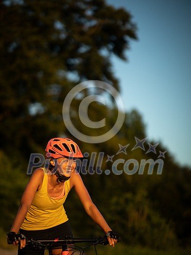 Pretty, young woman biking on a mountain bike enjoying healthy active lifestyle outdoors in summer (shallow DOF)