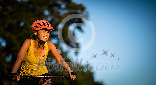 Pretty, young woman biking on a mountain bike enjoying healthy active lifestyle outdoors in summer (shallow DOF)