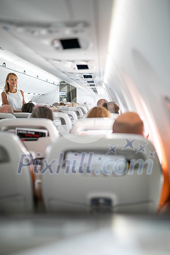 Pretty, young woman aboard an airplane during a lang haul commercial flight - stretching her legs a bit, walking in the aisle