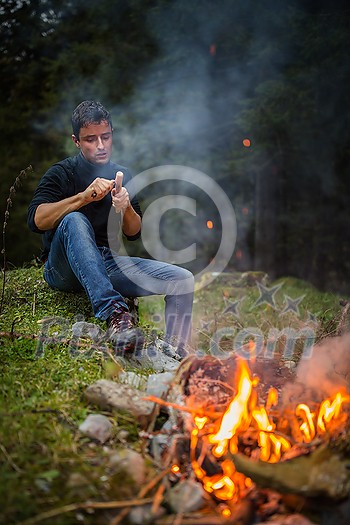 Young man making tools out of wood by a campfire