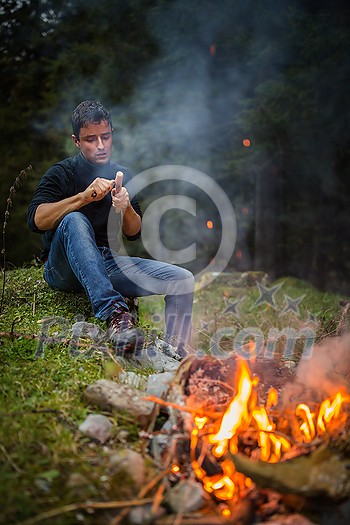 Young man making tools out of wood by a campfire Young man making tools out of wood by a campfire