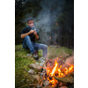 Young man making tools out of wood by a campfire