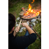 Young man making tools out of wood by a campfire