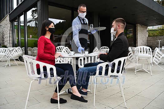 Waiter with protective medical mask and gloves serving guest with coffee at an outdoor bar café or restaurant new normal concept reopening after quarantine Waiter with protective medical mask and gloves serving guest with coffee at an outdoor bar café or restaurant new normal concept reopening after quarantine