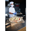 Skilled chef preparing traditional italian pizza  in interior of modern restaurant kitchen with special wood-fired oven. Wearing protective medical face mask and gloves in coronavirus new normal concept