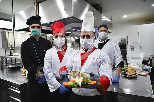 Mixed race team Portrait of group chefs standing together in the kitchen at restaurant wearing protective medical mask and gloves in coronavirus new normal concept