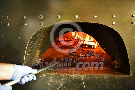 Skilled chef preparing traditional italian pizza in interior of modern restaurant kitchen with special wood-fired oven. Wearing protective medical face mask and gloves in coronavirus new normal concept Skilled chef preparing traditional italian pizza in interior of modern restaurant kitchen with special wood-fired oven. Wearing protective medical face mask and gloves in coronavirus new normal concept