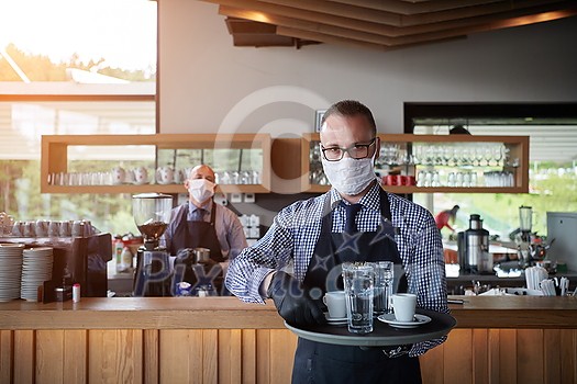 waiter in a medical protective mask serves the coffee in restaurant durin coronavirus pandemic representing new normal concept waiter in a medical protective mask serves the coffee in restaurant durin coronavirus pandemic representing new normal concept