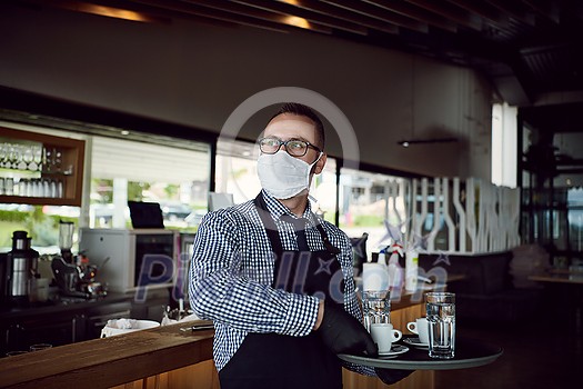 waiter in a medical protective mask serves the coffee in restaurant durin coronavirus pandemic representing new normal concept waiter in a medical protective mask serves the coffee in restaurant durin coronavirus pandemic representing new normal concept