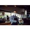 waiter in a medical protective mask serves  the coffee in restaurant durin coronavirus pandemic representing new normal concept