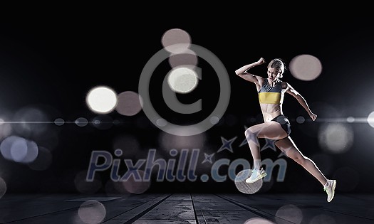 Young woman athlete running fast on dark background 