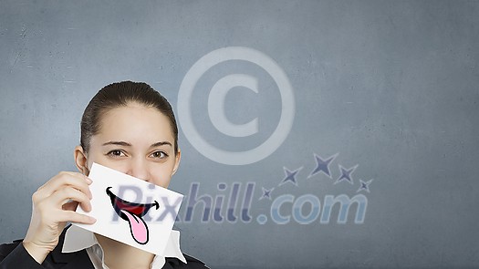 Pretty young girl holding white card with drawn smile showing tongue Pretty young girl holding white card with drawn smile showing tongue
