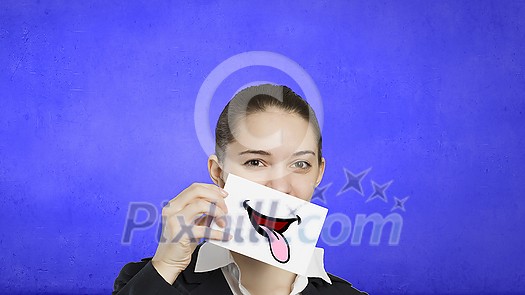 Pretty young girl holding white card with drawn smile showing tongue