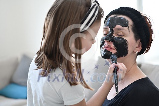 Family at home beauty treatment during coronavirus pandemic stay at home quarantine. Mother and little girl daughter  make a facial mask.