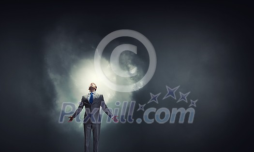 Businessman with hands spread apart standing in light coming from above Businessman with hands spread apart standing in light coming from above
