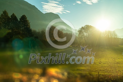 Beautiful natural countryside landscape with trees, mountains, green fields, areas and blurred forefront on a background of sunny blue sky, Austria.