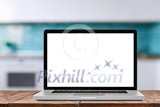 Empty white screen of modern laptop on a wooden table against blurred kitchen interior background, copy space. Working at home, outside office work concept. Empty white screen of modern laptop on a wooden table against blurred kitchen interior background, copy space. Working at home, outside office work concept.