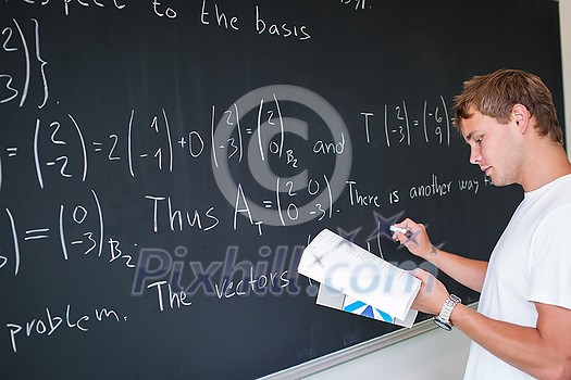 Handsome college student solving a math problem during math class in front of the blackboard/chalkboard (color toned image) Handsome college student solving a math problem during math class in front of the blackboard/chalkboard (color toned image)