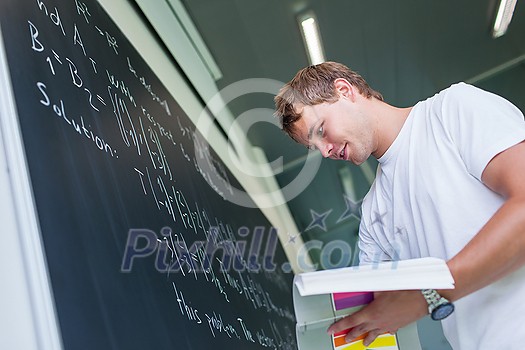 Handsome college student solving a math problem during math class in front of the blackboard/chalkboard (color toned image) Handsome college student solving a math problem during math class in front of the blackboard/chalkboard (color toned image)