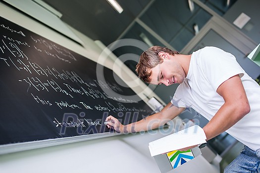 Handsome college student solving a math problem during math class in front of the blackboard/chalkboard (color toned image)