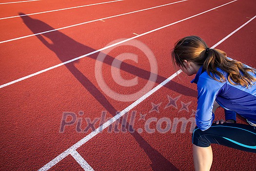 Pretty female runner stretching before her run at a track and field stadium