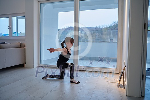 Little girl have online training while watching the tablet and doing fitness and modern ballet dance exercise at home. Online education concept class in modern ballet school. Social distance during quarantine, self-isolation in coronavirus pandemic staying at home time.
