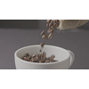 In a white cup, pour the roasted coffee beans from the bag around a dark background. Slow motion, Full HD video, 240fps, 1080p.