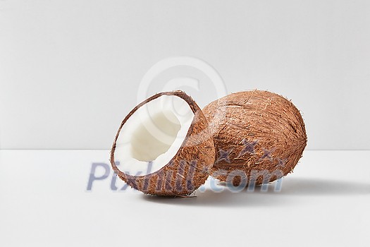 Whole natural exotic ripe coconut fruit with half on a duotone light grey background with soft shadows, copy space. Vegetarian concept. Whole natural exotic ripe coconut fruit with half on a duotone light grey background with soft shadows, copy space. Vegetarian concept.