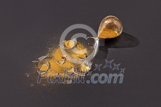 Old vintage crashed hourglass with glass shatters and golden sand on the black background with hard shadows, copy space. Old vintage crashed hourglass with glass shatters and golden sand on the black background with hard shadows, copy space.