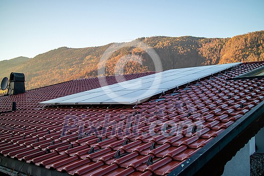 Alternative energy solar panels on a tiled roof on a background of stone mountains and clear blue sky in autumn day, Austria.