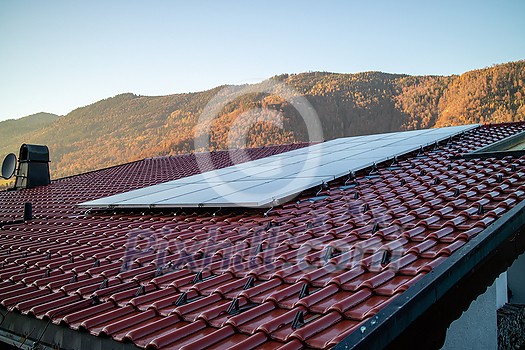 Alternative energy solar panels on a tiled roof on a background of stone mountains and clear blue sky in autumn day, Austria. Alternative energy solar panels on a tiled roof on a background of stone mountains and clear blue sky in autumn day, Austria.