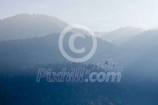 Beautiful tranquil landscape from blurred foggy mountains with trees on a background of sunny clear sky in Kufstein Austria.