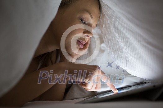 Pretty young woman using a tablet computer in bed
