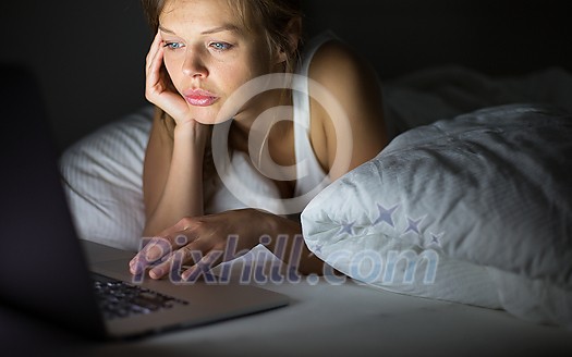 Pretty, young woman using her laptop computer in bed (color toned image; shallow DOF)