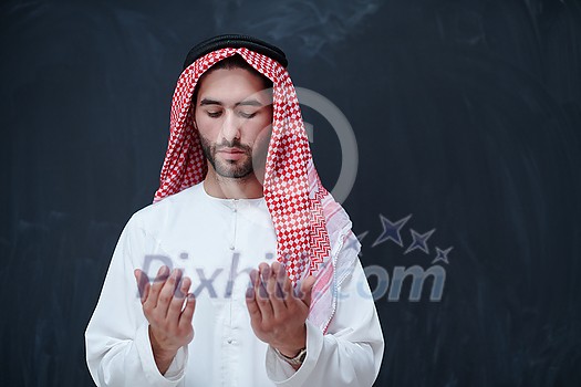 young arabian man in traditional clothes making traditional prayer to God, keeps hands in praying gesture in front of black chalkboard representing modern islam fashion and ramadan kareem concept young arabian man in traditional clothes making traditional prayer to God, keeps hands in praying gesture in front of black chalkboard representing modern islam fashion and ramadan kareem concept